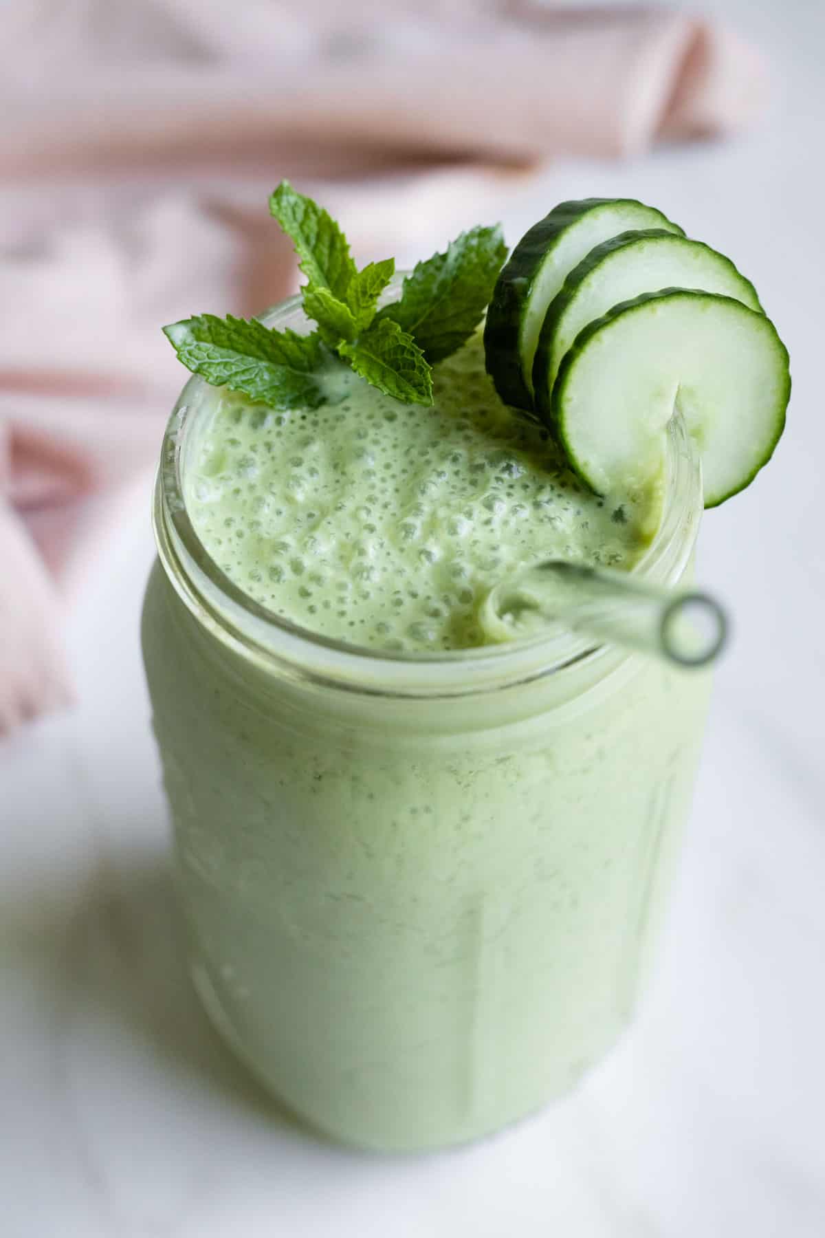 Looking down at a Ball jar filled with creamy spinach cucumber smoothie garnished with mint and a slice of cucumber.