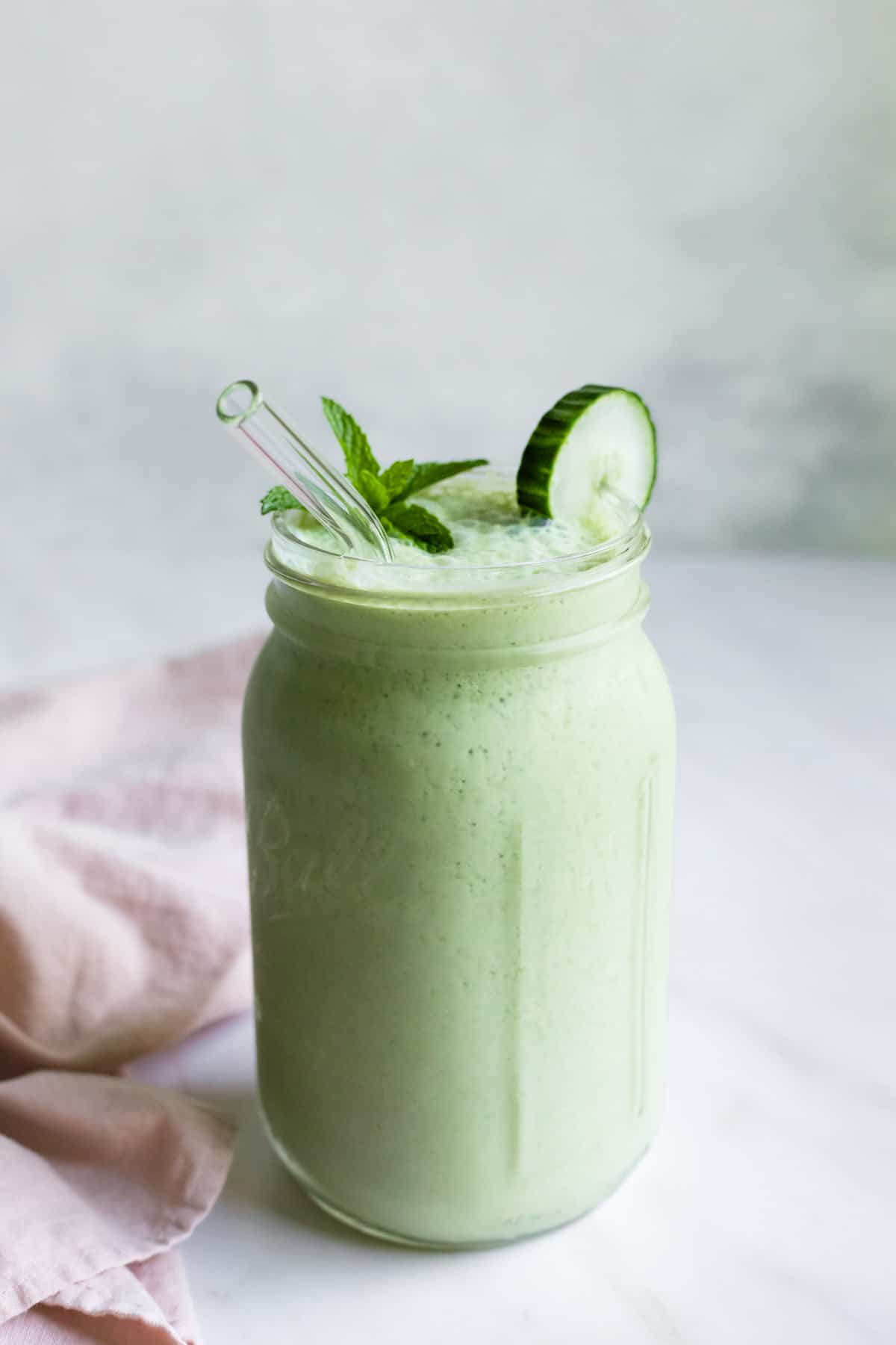 A large jar garnished with mint and a slice of cucumber and filled with cucumber smoothie.