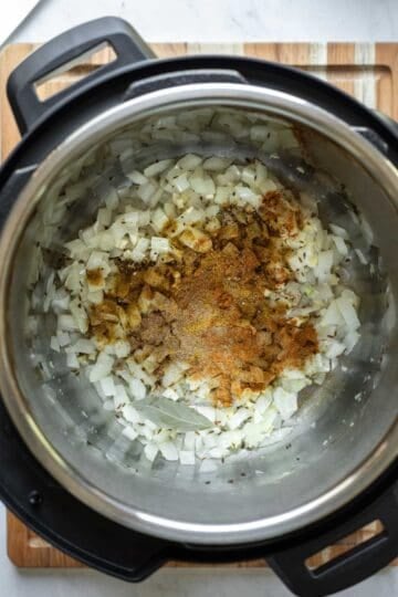 Adding spices and bay leaf to the kitchari base in the Instant Pot.