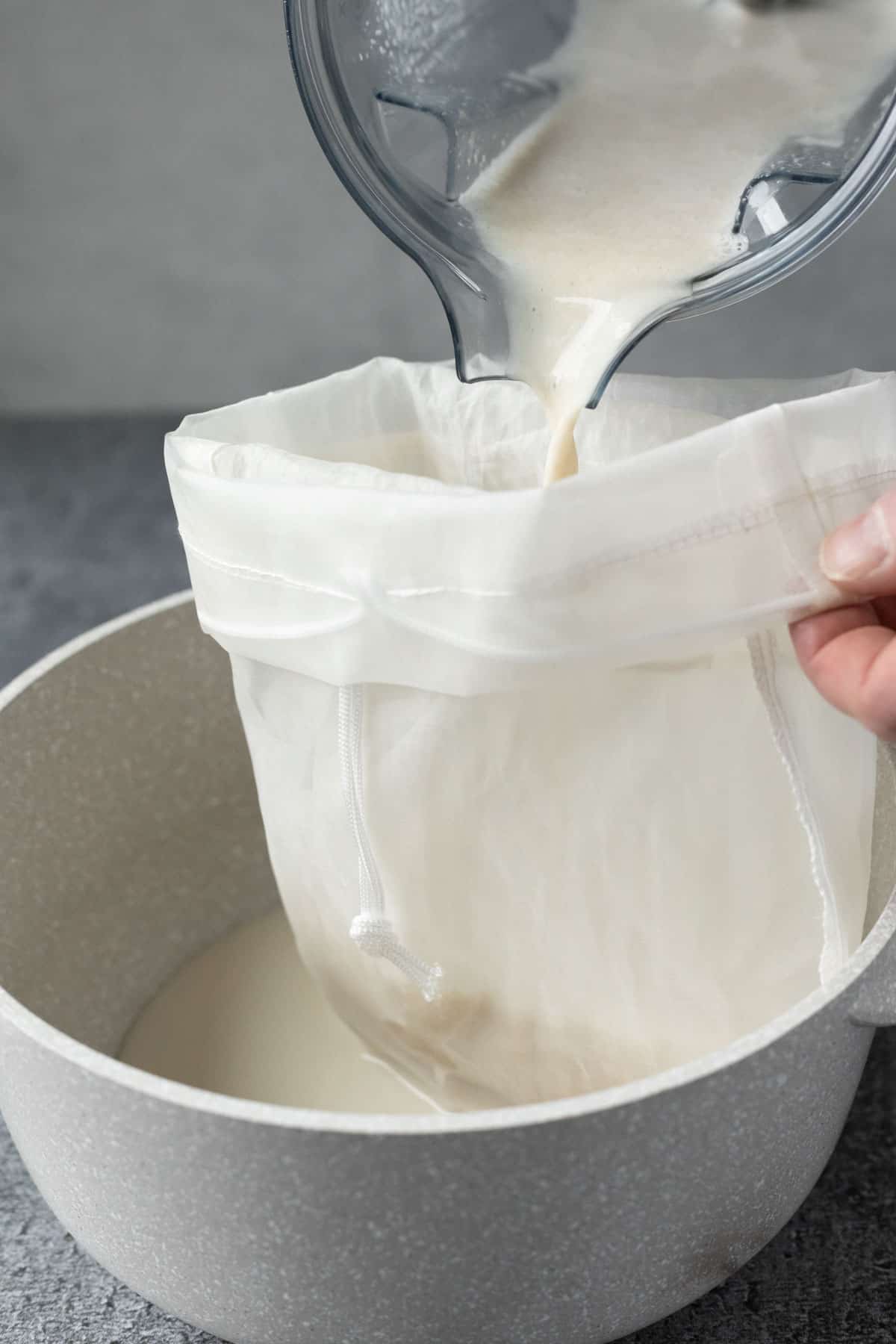 Pouring oat cream from a blender into a nut milk bag.