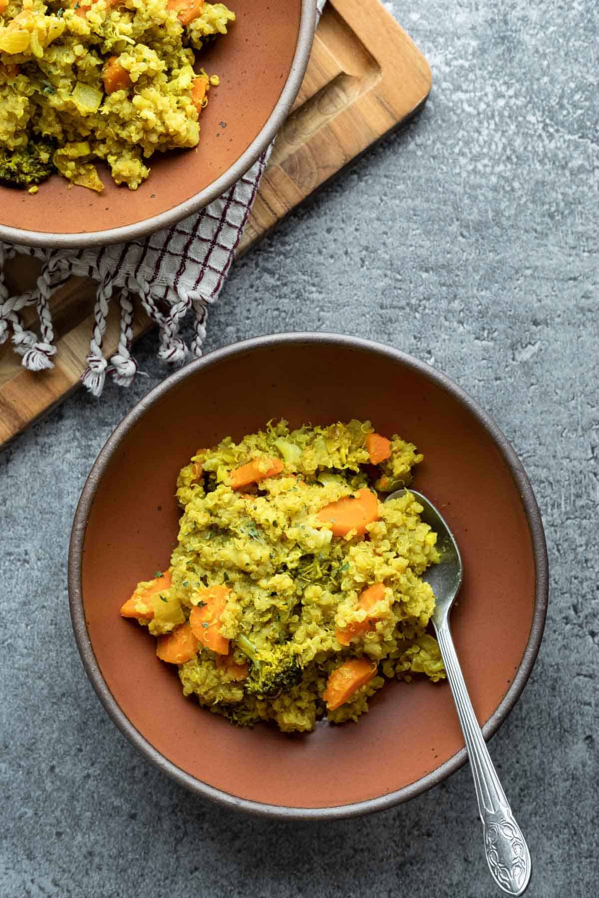 Two bowls filled with golden quinoa kitchari against a blue-gray background.