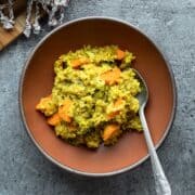 A red bowl filled with quinoa kitchari that includes carrot and broccoli.