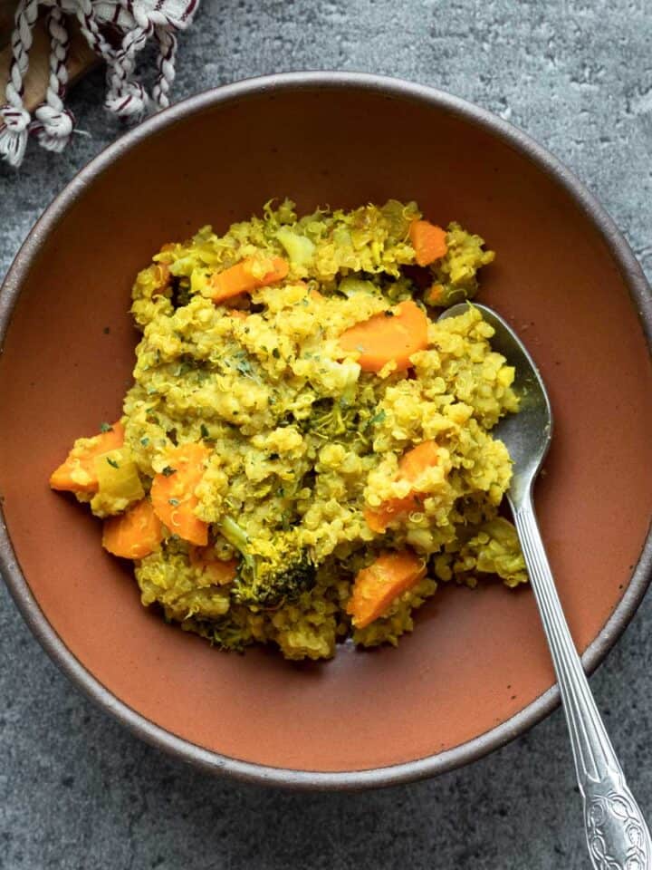 A red bowl filled with quinoa kitchari that includes carrot and broccoli.