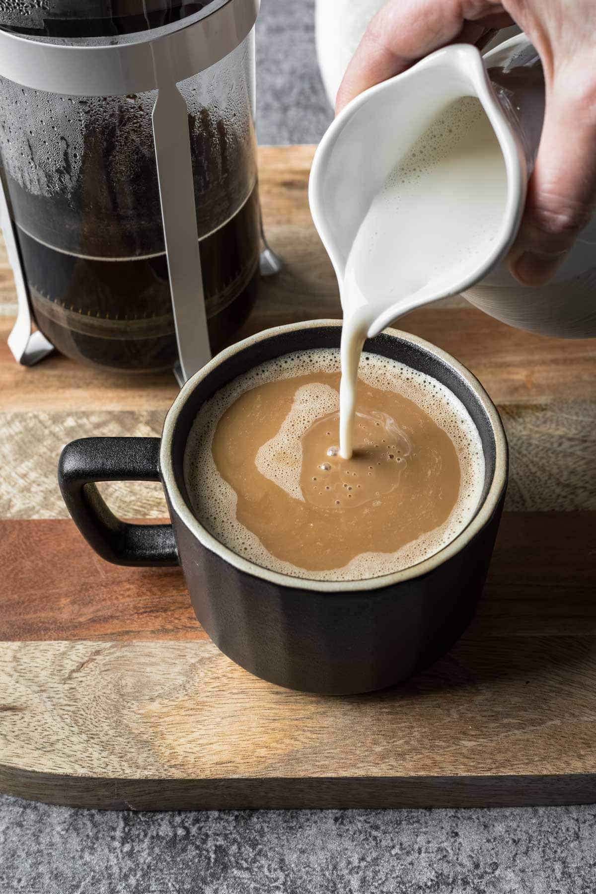 Pouring oat milk creamer from a jar into a mug of coffee.