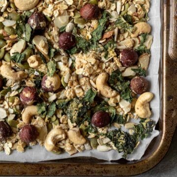 Crunchy granola made with rosemary and savory spices spread on a parchment-lined baking sheet.