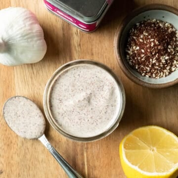 Dressing in a jar and on a small spoon with a cut lemon and za'atar seasoning nearby.