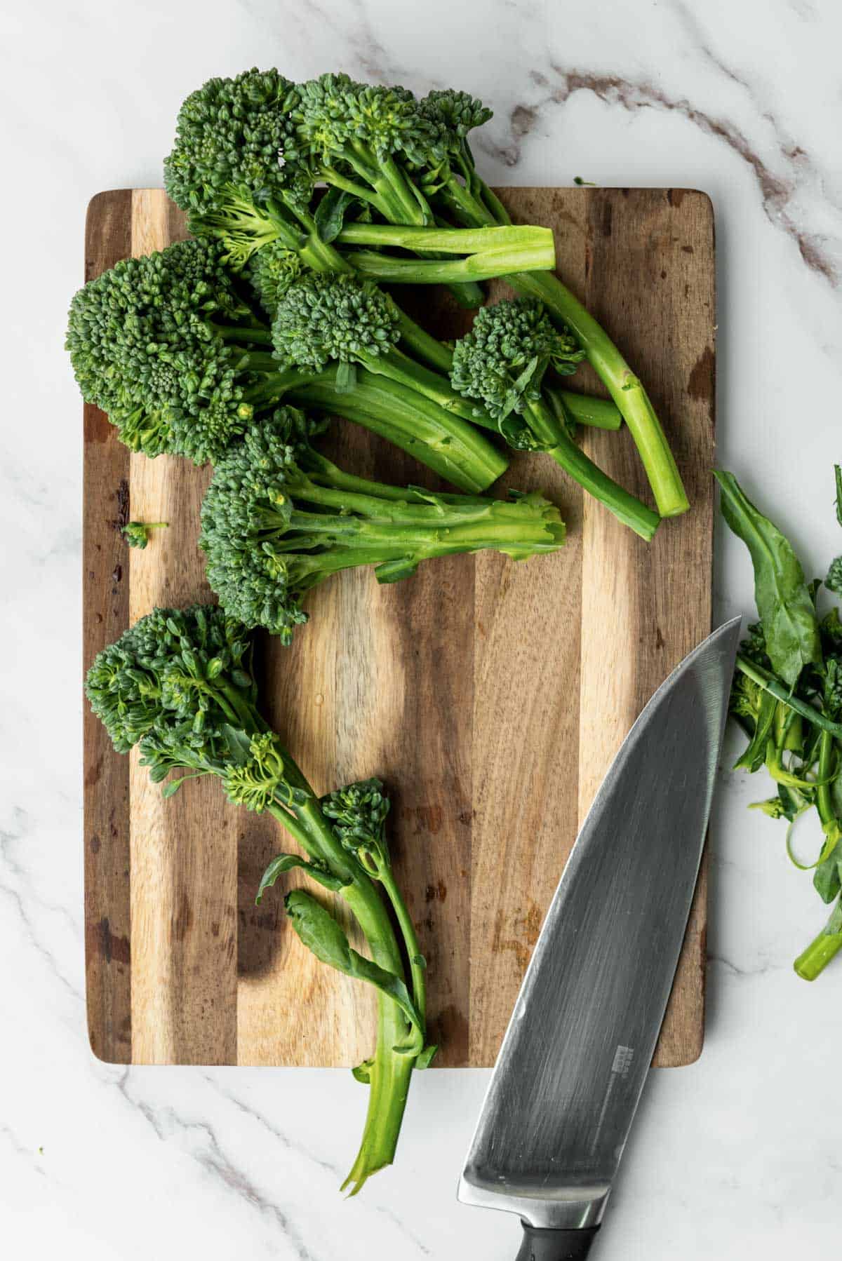 A large knife and broccolini resting on a wooden cutting board.
