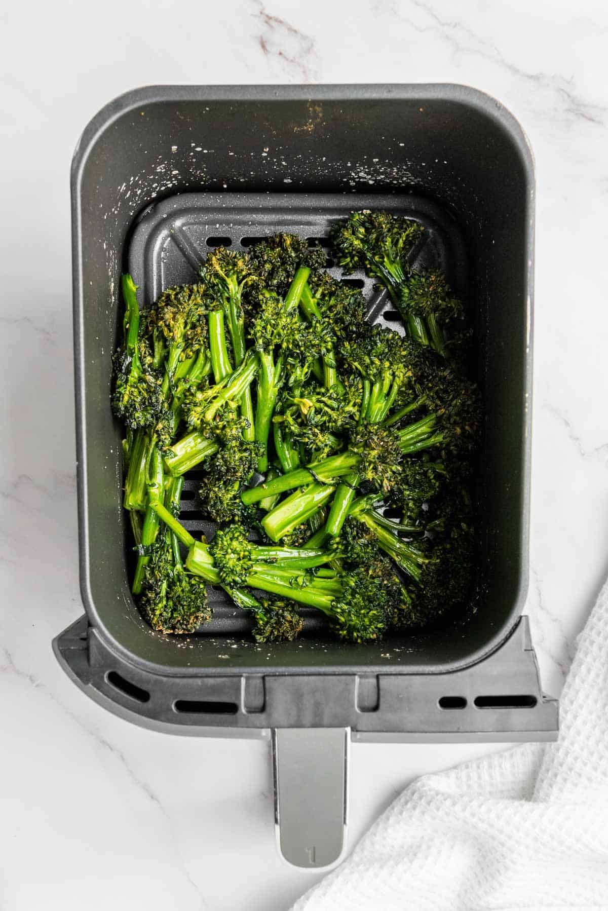 Looking inside the air fryer basket at freshly cooked broccolini.