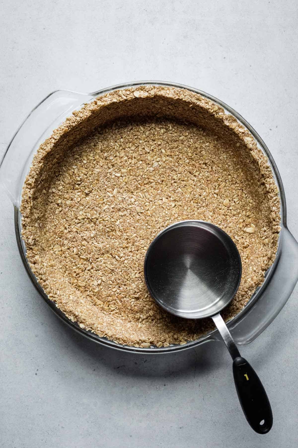 Using the bottom of a measuring cup to press the oat pie crust into the dish.
