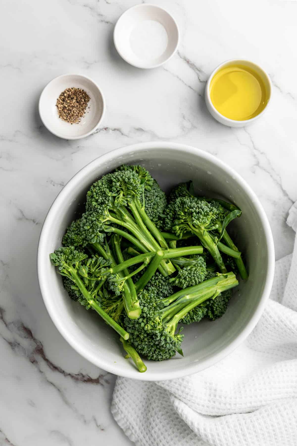 Washed and trimmed broccolini in a bowl with oil, salt, and pepper.