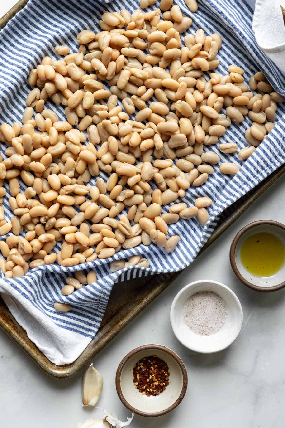 Cannelini beans spread out on a towel with oil, salt, and pepper nearby.