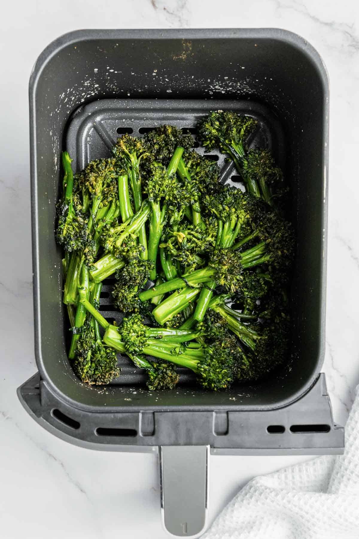 Tender broccolini inside an air fryer basket.