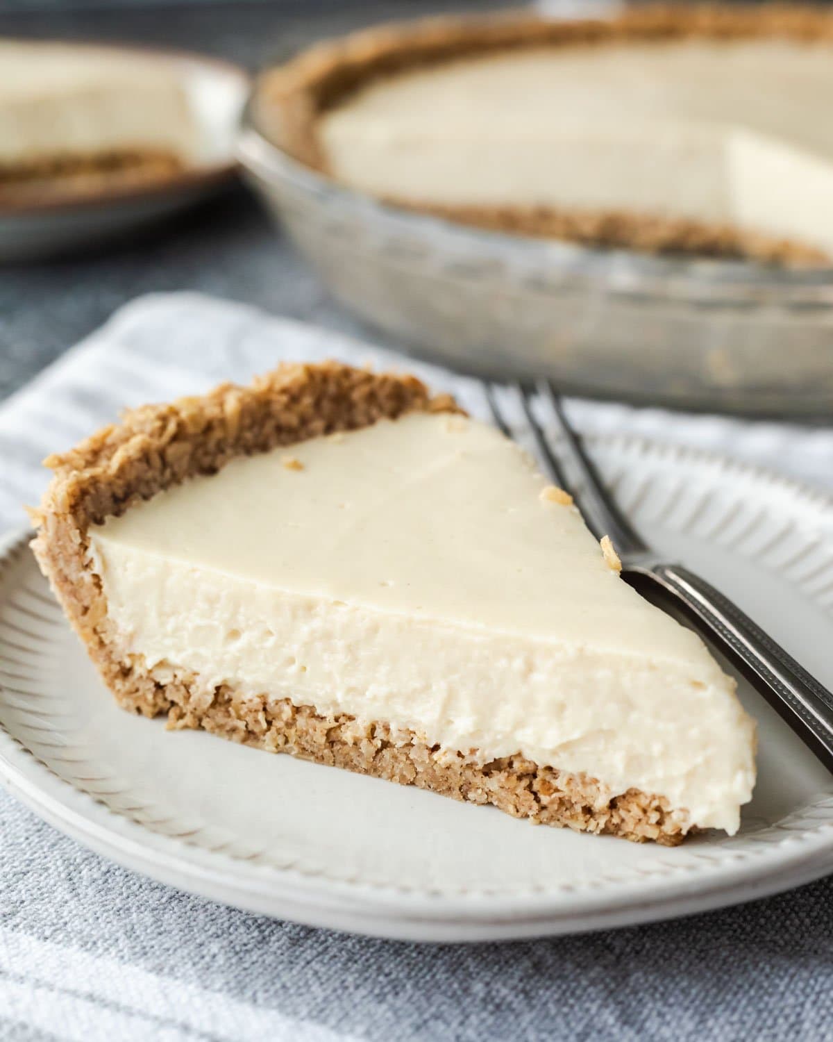 A slice of creamy vegan cheesecake on a plate showing the oatmeal pie crust texture.