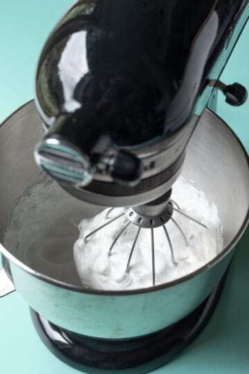 Fully whipped aquafaba at stiff peaks stage inside the bowl of a stand mixer.