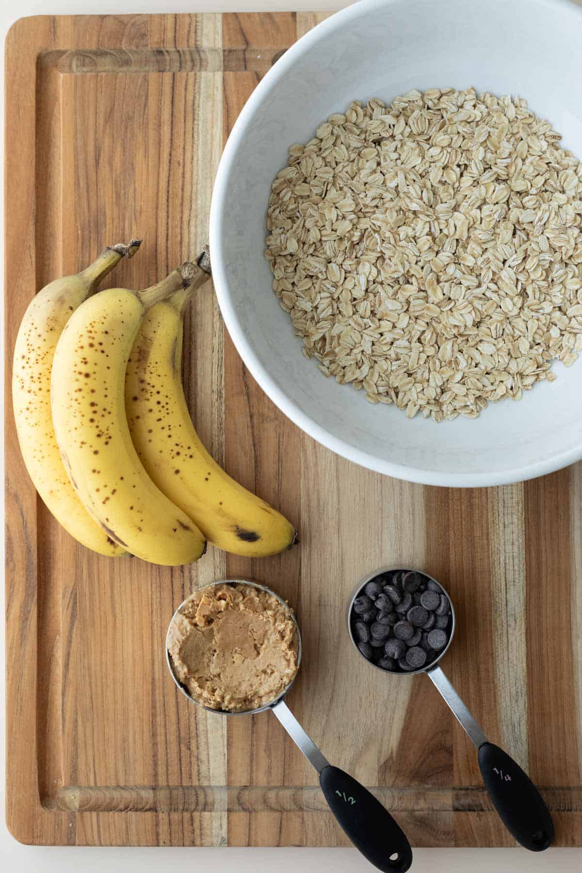 Ingredients needed for banana peanut butter cookies laid out on a wood cutting board.