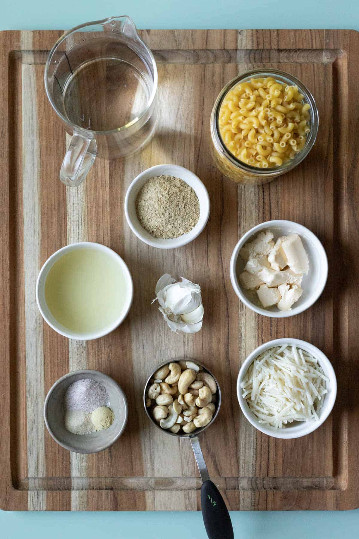 The 9 ingredients needed for vegan Crockpot mac and cheese on a wood cutting board.