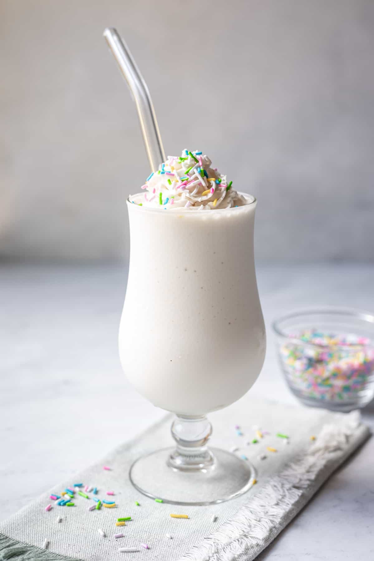 Creamy vegan milkshake in a tall glass topped with non-dairy Redi-wip and pastel sprinkles.