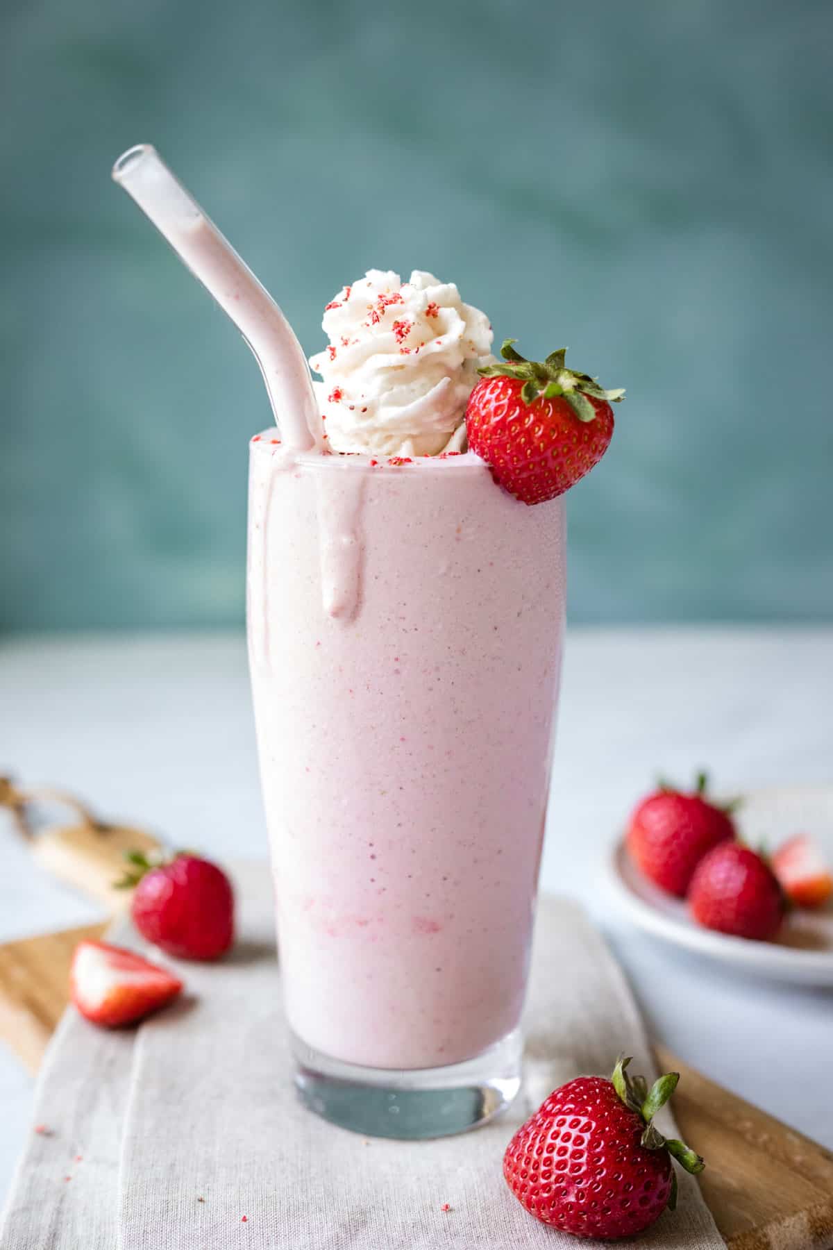 Vegan strawberry milkshake in a tall glass garnished with whipped cream and fresh strawberries.