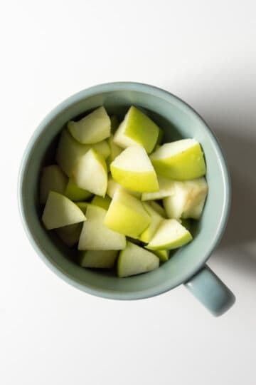 Chopped apples in a teal colored mug.