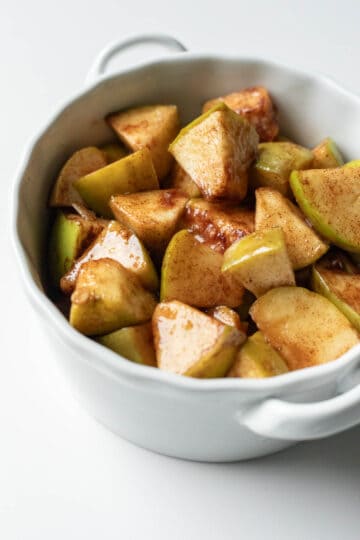 Layering spiced apples in a large white bowl to cook in the microwave.