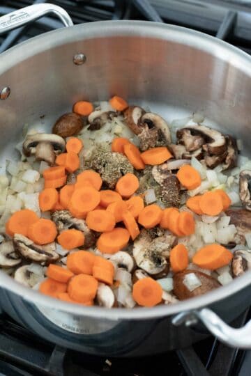 Adding dried herbs and carrots to the pot with the onion and mushrooms.