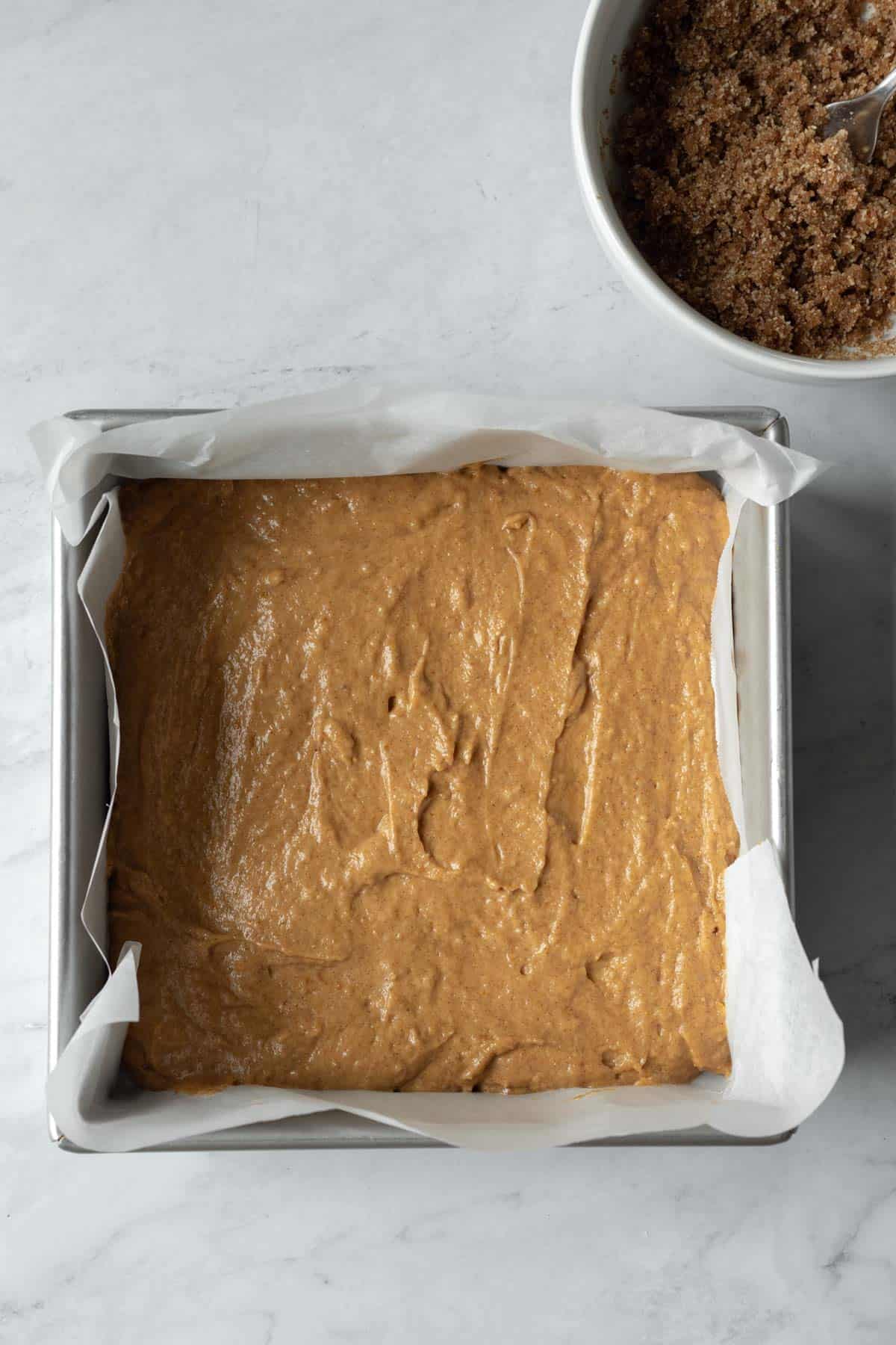 Thick coffee cake batter spread out in a square baking pan.