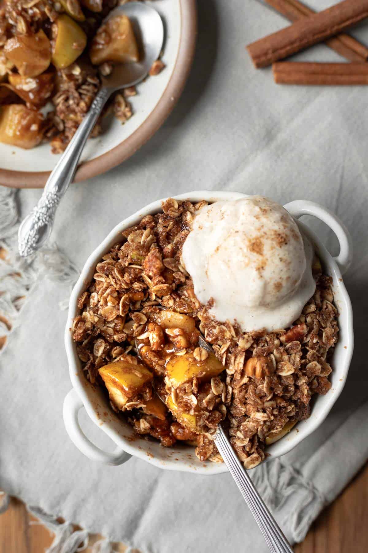 A spoon digging into microwave apple crisp topped with dairy-free vanilla ice cream.