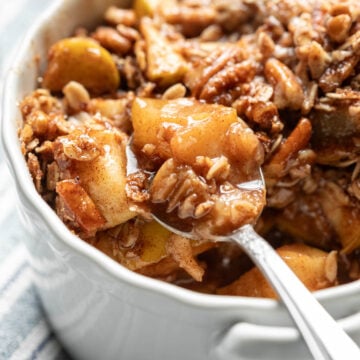 Bright photo of a spoon scooping up vegan apple crisp made in the microwave, topped with a crunchy pecan-oat topping.