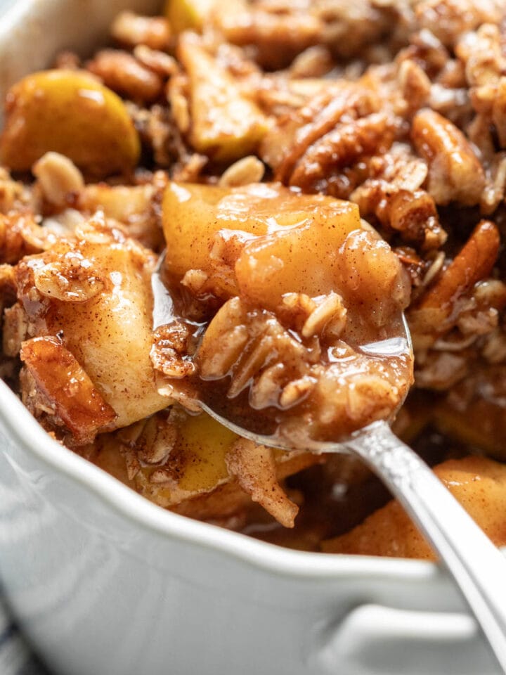Bright photo of a spoon scooping up vegan apple crisp made in the microwave, topped with a crunchy pecan-oat topping.