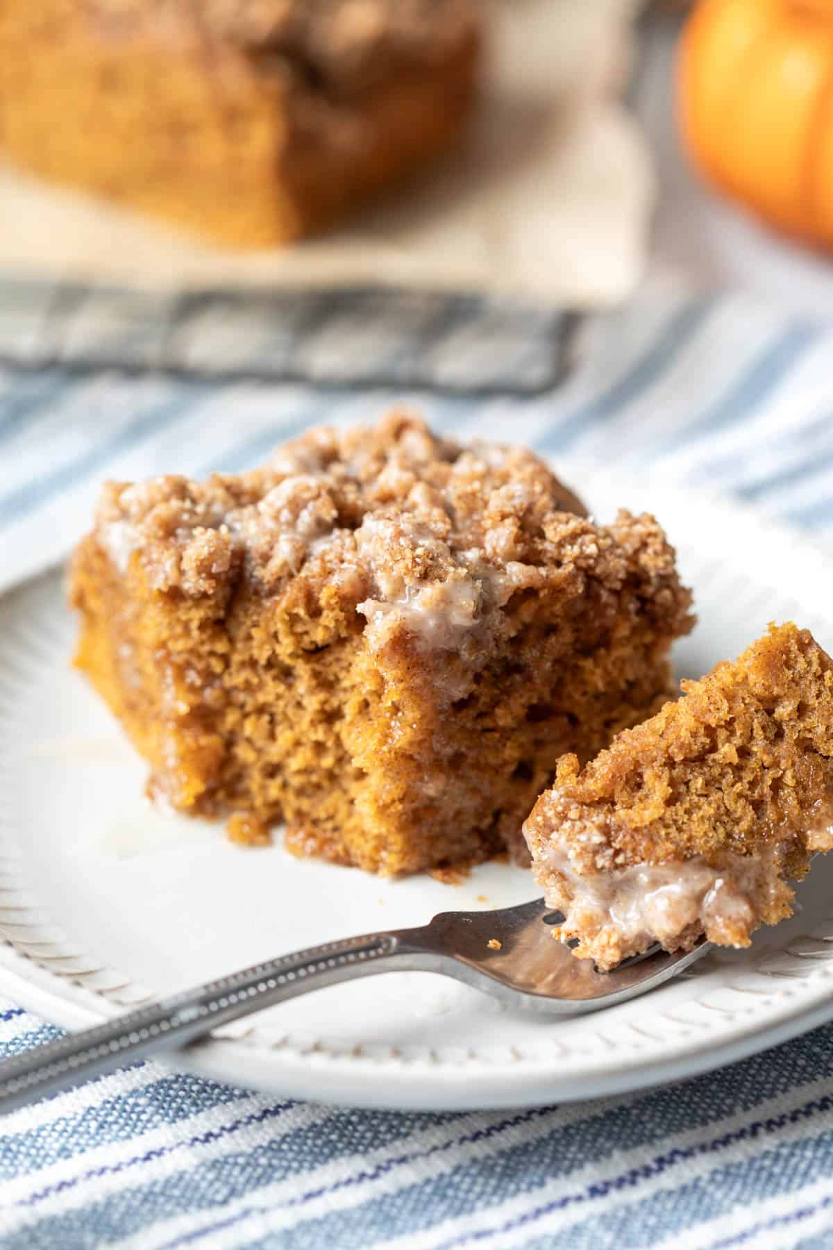 A moist bite of vegan pumpkin cake resting on a fork next to whole piece showing texture.