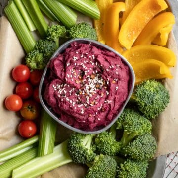 Purple dip in a bowl surrounded by colorful raw veggies.