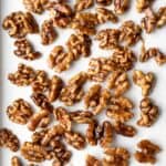 Glazed maple walnuts cooling on a parchment-lined baking sheet.