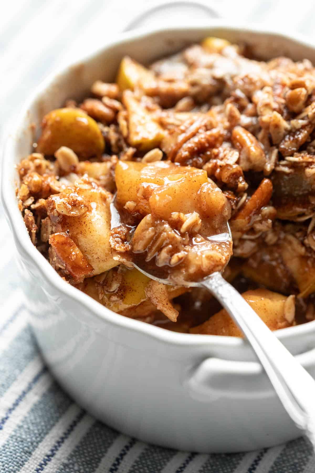 Bright backlit photo of microwaved apple crisp in a white bowl.