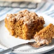 A piece of pumpkin cake on a small plate with a bite resting on a fork.