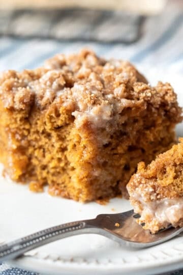 A piece of pumpkin cake on a small plate with a bite resting on a fork.