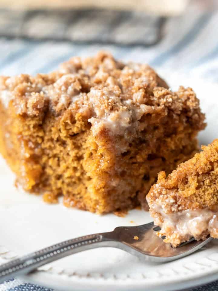 A piece of pumpkin cake on a small plate with a bite resting on a fork.