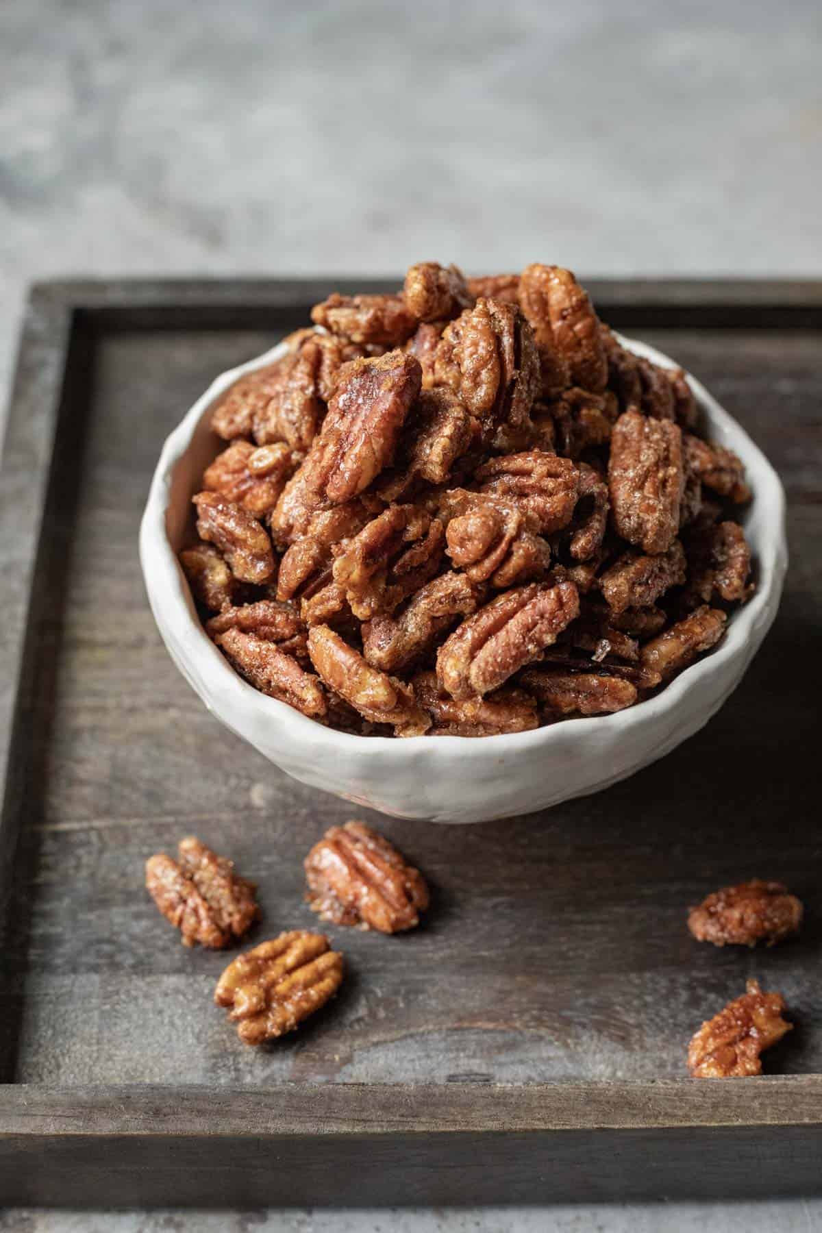 Homemade bourbon candied pecans in a small serving bowl on a wood platter.