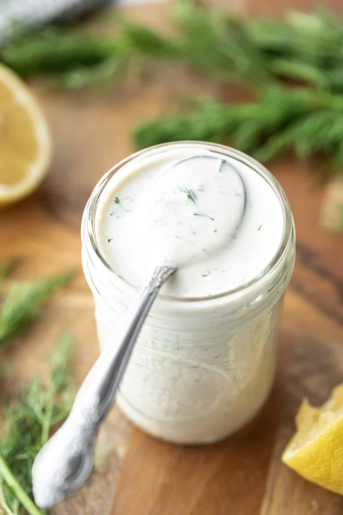 Creamy dill dressing in a glass jar with a spoon resting on top and fresh dill nearby.