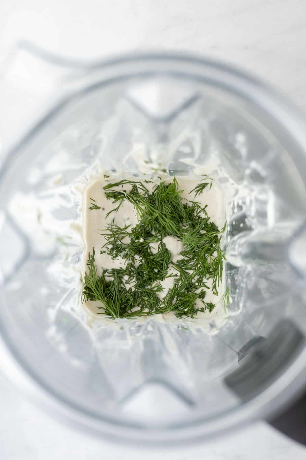 Looking inside a blender with fresh dill added to the dressing.