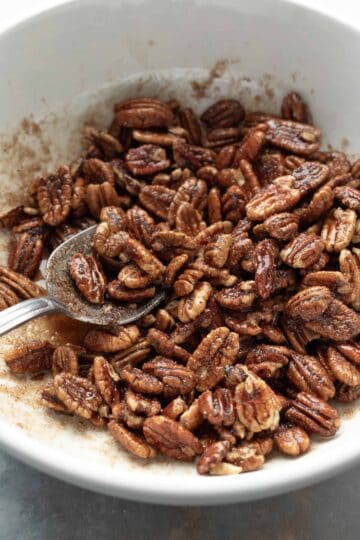 Stirring pecans and sugary coating together in a mixing bowl.