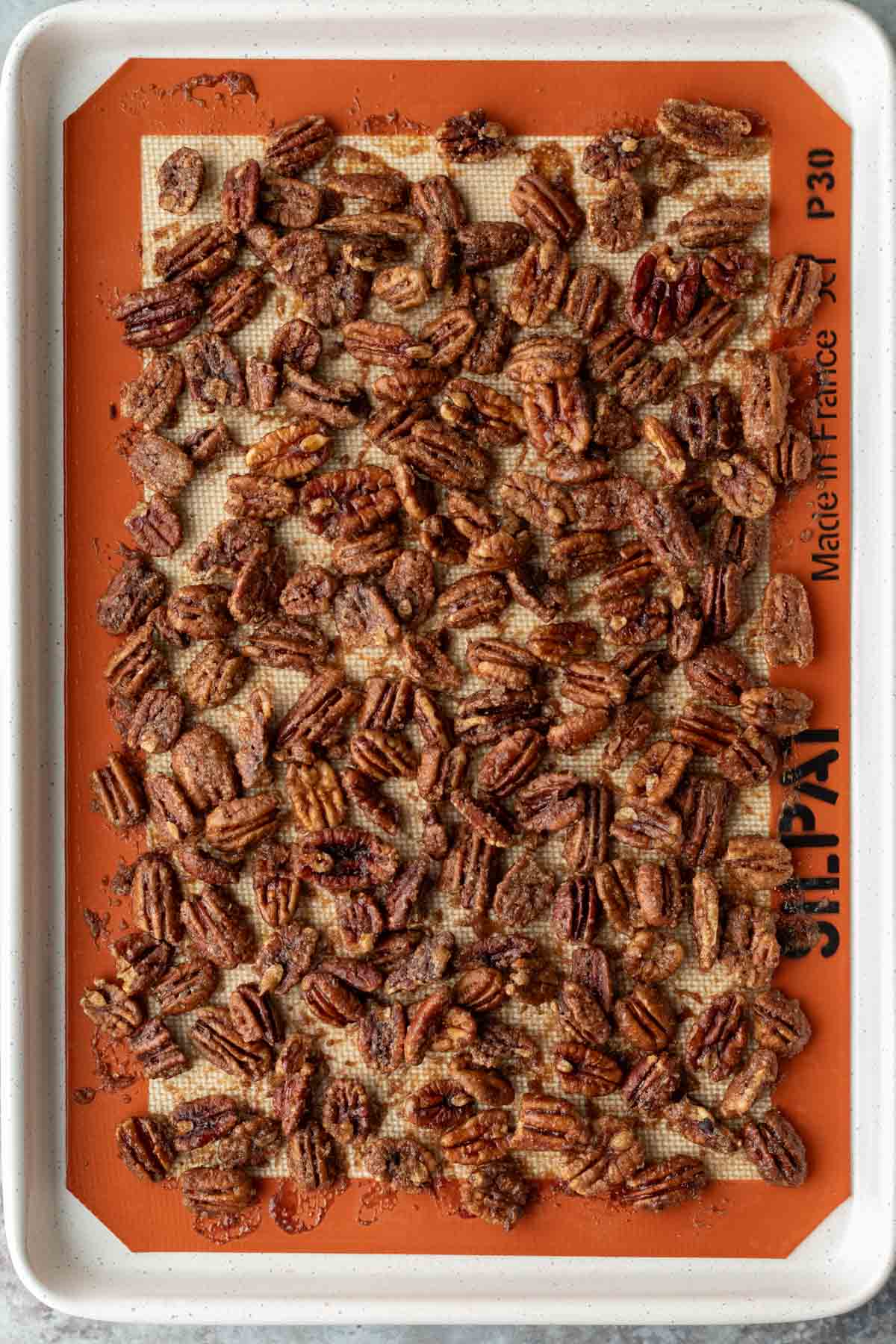 Freshly baked candied pecans cooling on a baking sheet.