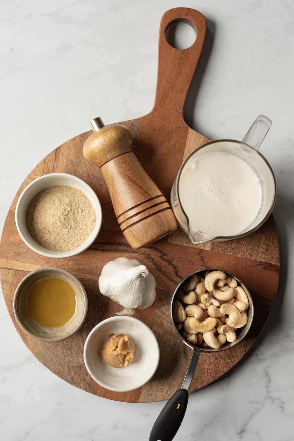 The 7 ingredients needed to make dairy free bechamel sauce laid out on a wood board.