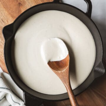 Creamy white bechamel sauce in a pan with a wooden spoon resting.