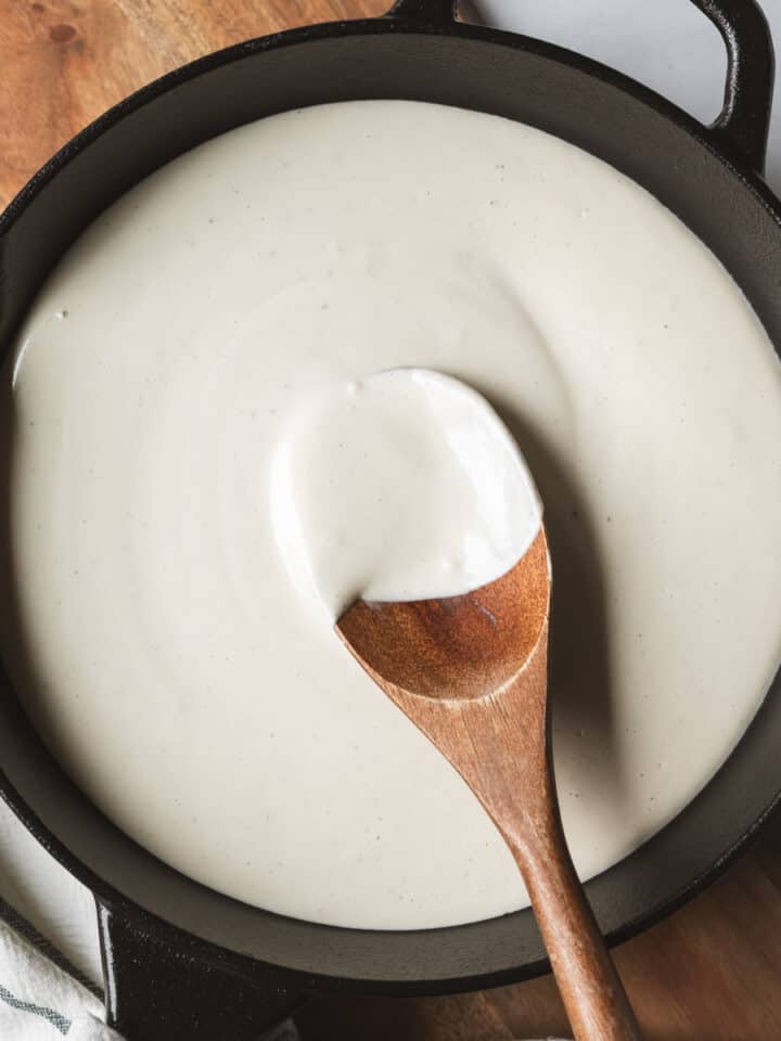 Creamy white bechamel sauce in a pan with a wooden spoon resting.