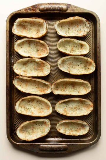 Hollowed out potatoes lined up on a baking sheet.