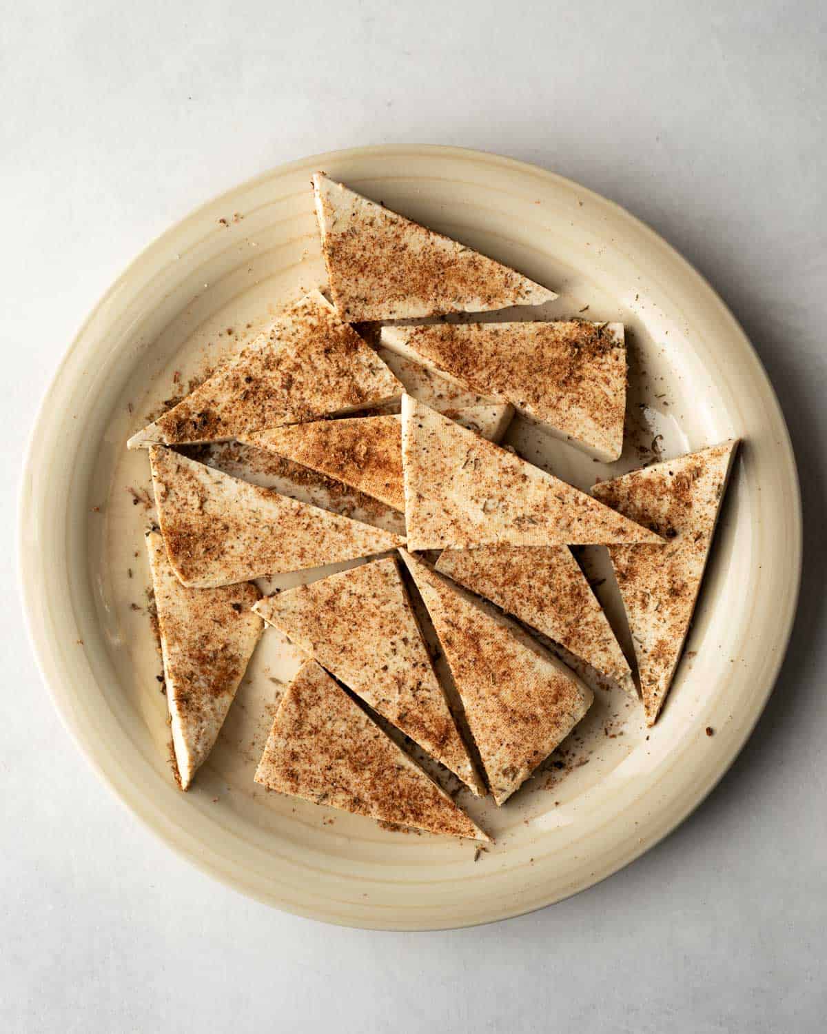 Coating tofu triangles with a spice-herb dry rub.