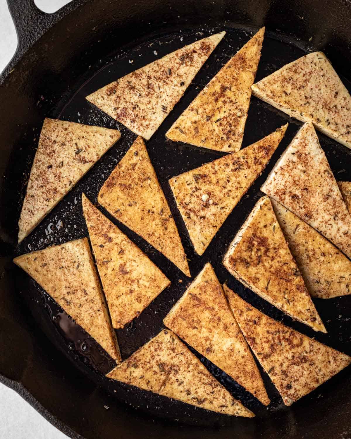 Tofu coated in a dry spice rub is seared in a large cast iron skillet.