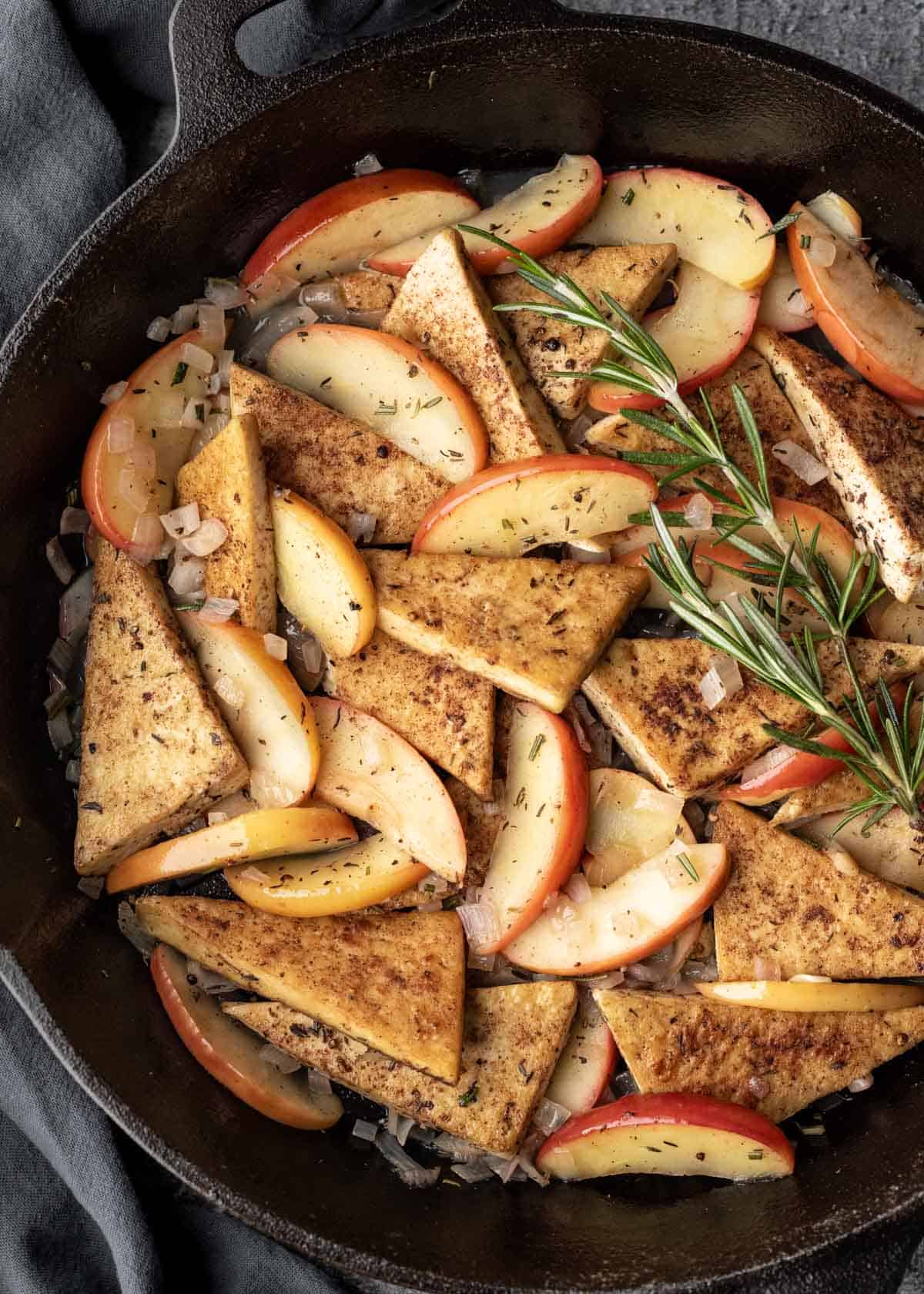Apple cider tofu made with fresh apples, shallot, and herbs in a large cast iron skillet.