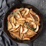 A large skillet filled with tofu, apples, rosemary, and shallot, and glazed with apple cider.