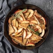A large skillet filled with tofu, apples, rosemary, and shallot, and glazed with apple cider.